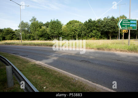 Cattiva strada su superfici di le strade della Gran Bretagna. Giunzione di Pyebush rotonda e A355, Beaconsfield. Rivolta verso il filo di acciaio inossidabile. Foto Stock