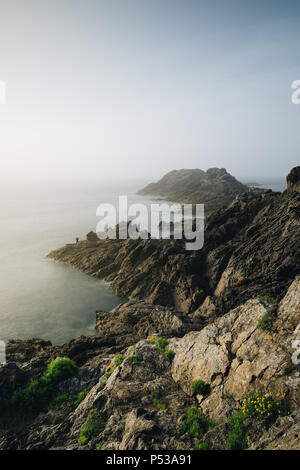 Pescatore solitario in piedi sulle rocce al tramonto. Pointe du Grouin in Bretagne. Foto Stock