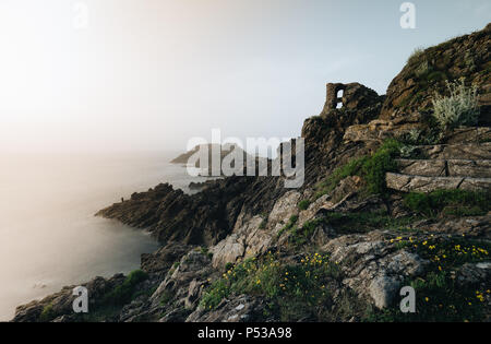 Pescatore solitario in piedi sulle rocce al tramonto. Pointe du Grouin in Bretagne. Foto Stock