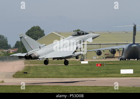 Royal Air Force Typhoon FGR4 sopra la pista e attorno alla terra a RAF Coningsby, casa di base. Nota Il USAF C-17 trasporto parcheggiato dietro. Foto Stock