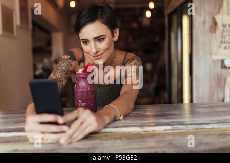 Donna prendendo un selfie con un smoothie collocato di fronte a lei utilizzando un telefono cellulare per il suo cibo blog. Blogger alimentare a scattare foto per il suo blog a casa Foto Stock