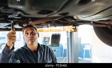 Esperto meccanico auto riparazione di un sollevato auto in garage. Riparazione auto di uomini che fissa il sistema di scarico di un'auto. Foto Stock