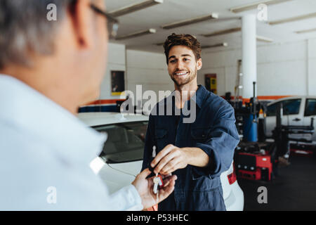 Autofficine passando le chiavi dell'auto al proprietario del veicolo dopo la riparazione del suo veicolo. Mechanic dando chiave auto al cliente dopo la manutenzione al garage. Foto Stock