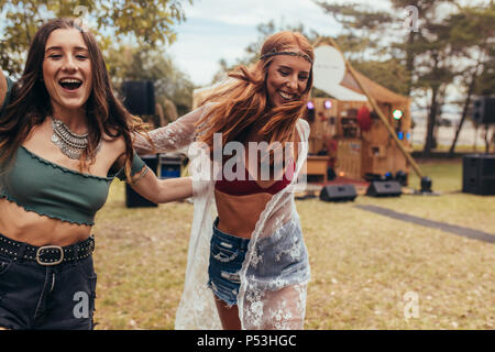 Due giovani donne a piedi e ballare nel parco. Hipsters godendo una giornata al parco durante il festival di musica. Foto Stock