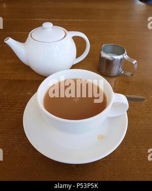 Tazza da tè riempita con tè sul piattino con tè pentola e latte su un tavolo Foto Stock