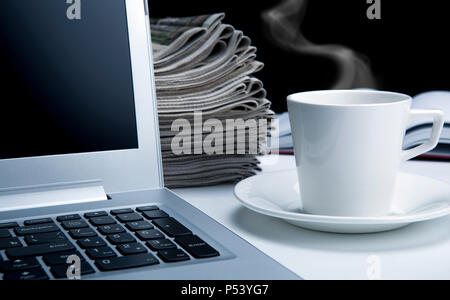 Computer e quotidiani sul desktop e una tazza di tè Foto Stock