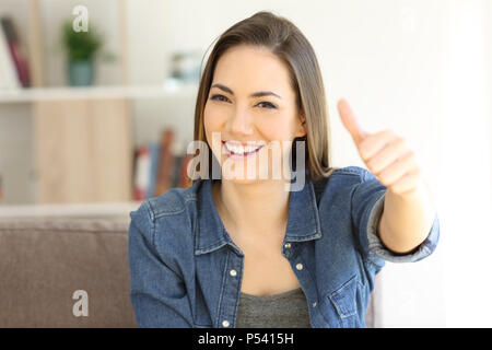 Vista frontale il ritratto di una donna felice gesticolando Thumbs up seduto su un divano nel salotto di casa Foto Stock