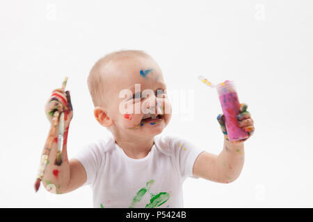 Carino piccolo bambino pittura con pennello e vernici colorate in bianco. Isolato in uno sfondo bianco. Foto Stock