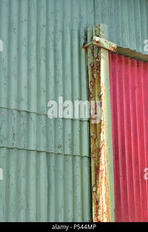 Verde chiaro e rosso parete esterna realizzata in lamiera grecata con alcune macchie di ruggine. Foto Stock