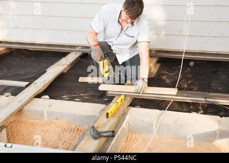 L'uomo carpenter l'installazione di un pavimento in legno terrazza esterna in casa di nuova costruzione sito. Lo stile scandinavo Foto Stock