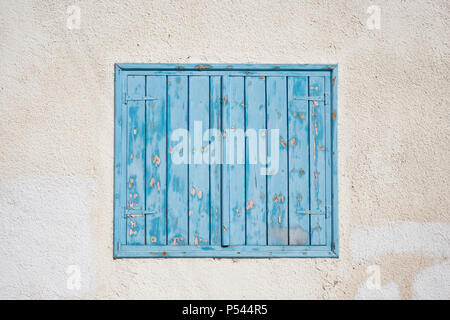 Cipro, Larnaca. In legno di colore blu, sbucciate finestra, che le imposte sulla parete rosa. Facciata del vecchio edificio in pietra, primo piano. Foto Stock