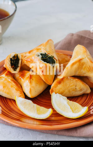In arabo e in Medio Oriente il concetto di cibo. Fatayer sabanekh - arabo tradizionale triangolo di spinaci torte di mano su una pietra bianca dello sfondo. Foto Stock