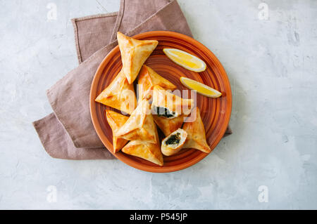 In arabo e in Medio Oriente il concetto di cibo. Fatayer sabanekh - arabo tradizionale triangolo di spinaci torte di mano su una pietra bianca dello sfondo. Foto Stock