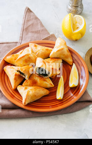 In arabo e in Medio Oriente il concetto di cibo. Fatayer sabanekh - arabo tradizionale triangolo di spinaci torte di mano su una pietra bianca dello sfondo. Foto Stock