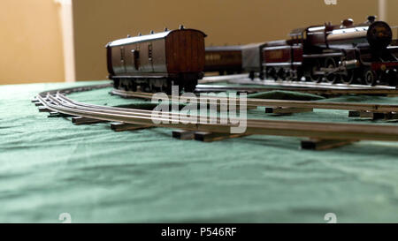 Primo piano vintage modello treno elettrico formato da una locomotiva a vapore e un verde le autovetture in esecuzione su rotaie. Foto Stock