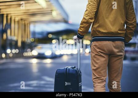 A piedi passeggero al di fuori del terminal dell'aeroporto. Vista posteriore del giovane uomo con i bagagli di notte. Foto Stock