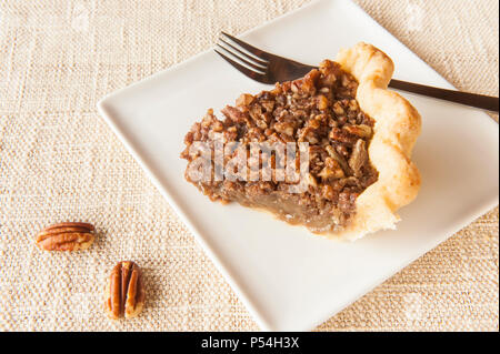 Una fetta di torta alle noci pecan su un quadrato bianco con piastra intera di noci pecan Foto Stock