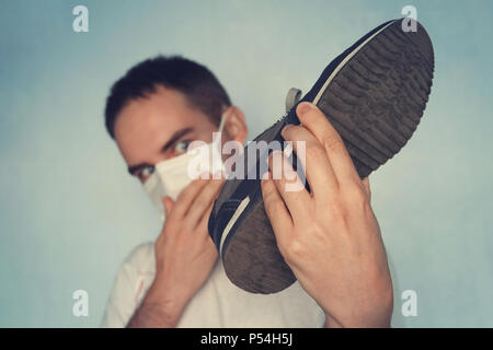 L'uomo con la maschera è azienda sporca puzzolente e cassoncino di pulizia - odore sgradevole concetto, sporca e puzzolente sneakers. Guarda le sneakers Foto Stock