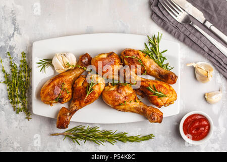 Speziato alla griglia cosce di pollo al forno con aglio, rosmarino e timo in piatto bianco su sfondo bianco. Foto Stock