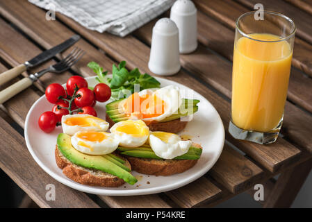 Toast con avocado, uova e un bicchiere di succo di arancia su di un tavolo di legno. Mangiare sano, uno stile di vita sano concetto Foto Stock