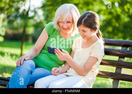 Nonna e nipote sono seduti in posizione di parcheggio e utilizzando il telefono cellulare. Foto Stock