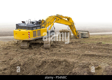 Escavatore giallo a argilloso sito in costruzione, parzialmente isolato in retro bianco Foto Stock