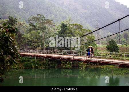 Ha Giang, Vietnam - Marzo 17, 2017: persone su una moto attraversando un piccolo ponte sospeso su di un fiume nella regione più settentrionale del Vietnam Foto Stock