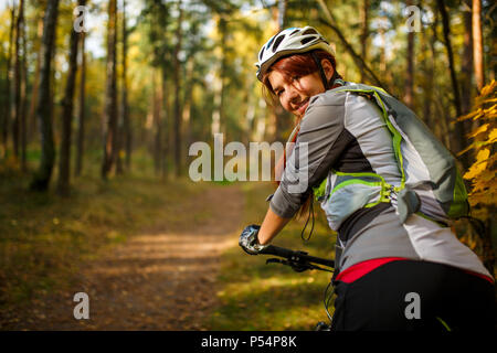 Foto di donna che indossa il casco in bicicletta nella foresta di autunno Foto Stock