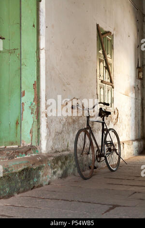 Vecchia moto puntellato contro la parete di un edificio coloniale, Kochi, Kerala, India SW. Foto Stock