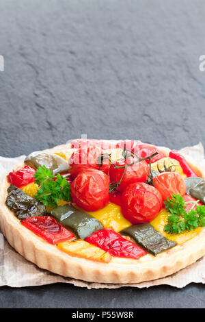 Quiche vegetariana con pepe colorato e i pomodori ciliegia sulla pietra nera sullo sfondo Foto Stock