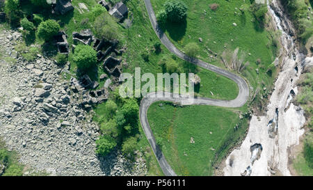 Antenna: vista dall'alto in basso tailspin su strada di montagna sulle Alpi italiane, attraversando il verde prato e pascolo nella valle alpina, avventura viaggio su strada Foto Stock