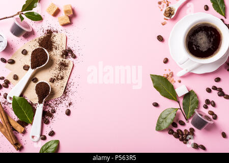 Il cibo lo sfondo con il caffè macinato in cucchiai di caffè in grani, tazzina, massa e capsule, foglie verdi copia spazio, vista dall'alto. Foto Stock