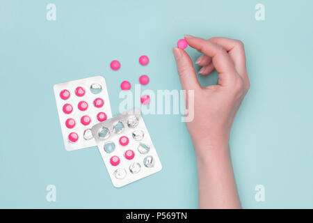 Vista superiore di femmine della mano che tiene la prescrizione di rosa confetto accanto a blister pastello su sfondo blu. Malato la somministrazione dei farmaci. Foto Stock