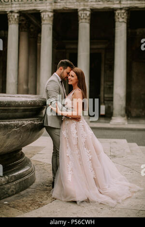 Attraente di giovani sposi passeggiate a piedi e in posa di Roma con la splendida e antica architettura sullo sfondo il giorno delle nozze Foto Stock