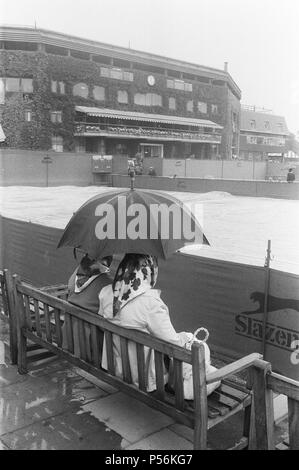 Wet Weather smette di giocare a Wimbledon. Fan affezionati sedersi fuori che il maltempo con la loro comune ombrello, con il Centre Court in background. La foto è stata scattata il 24 giugno 1983 Foto Stock