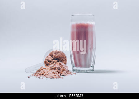 Fatta fresca la proteina del siero di latte shake in un bicchiere e scoop di polvere fine sul tavolo bianco. Integratori sport drink. Foto Stock