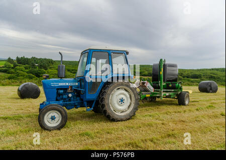 Ballydehob, West Cork, Irlanda. Il 25 giugno, 2018. Alan Pyburn di Durrus basato John O'Driscoll silaggio appaltatori avvolge un insilato bail sul Ballydehob farm di Ben Deane in una giornata molto calda. Questo è il preludio a una mini-ondata di caldo in cui le temperature sono impostati per raggiungere 31° gradi centigradi da giovedì di questa settimana. Credito: Andy Gibson/Alamy Live News. Foto Stock