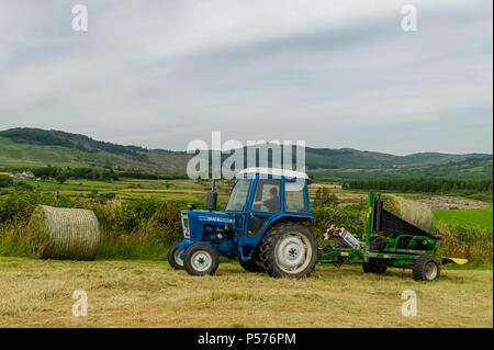 Ballydehob, West Cork, Irlanda. Il 25 giugno, 2018. Alan Pyburn di Durrus basato John O'Driscoll silaggio appaltatori avvolge un insilato bail sul Ballydehob farm di Ben Deane in una giornata molto calda. Questo è il preludio a una mini-ondata di caldo in cui le temperature sono impostati per raggiungere 31° gradi centigradi da giovedì di questa settimana. Credito: Andy Gibson/Alamy Live News. Foto Stock