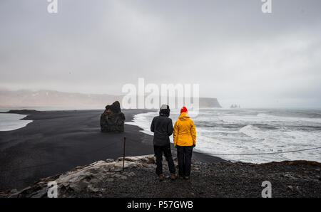 Due turisti che si affaccia su una spiaggia di sabbia nera, intemperie Reynisfjara Beach, Sud Islanda Islanda Foto Stock