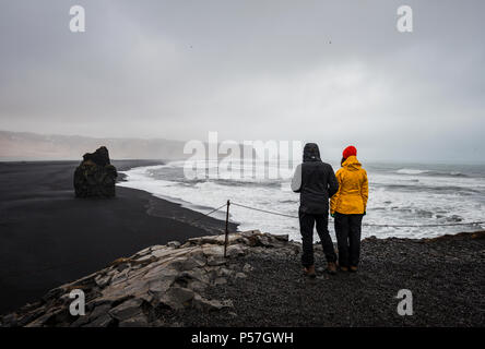 Due turisti che si affaccia su una spiaggia di sabbia nera, intemperie Reynisfjara Beach, Sud Islanda Islanda Foto Stock