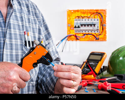 Elettricista tecnico al lavoro con spelafili su cavi in una zona residenziale di installazione elettrica. Foto Stock