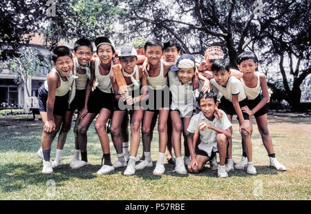 Dodici giovani scolari prendere una pausa dai giochi di posa per una foto di gruppo a Singapore, multirazziale e multiculturale del sudest asiatico con il paese di etnia cinese, degli Indiani e Malays che costituiscono la maggioranza della popolazione. Foto Stock