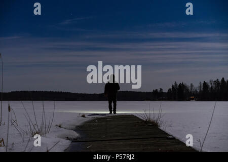 Umano all'aperto permanente di notte con torcia e felpa con cappuccio sulla testa. Voce maschile man standing in svedese Scandinavian la natura e il paesaggio luminoso con torcia. Foto Stock