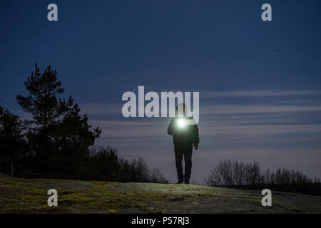 Umano all'aperto permanente di notte con torcia e felpa con cappuccio sulla testa. Voce maschile man standing in svedese Scandinavian la natura e il paesaggio luminoso con torcia. Foto Stock