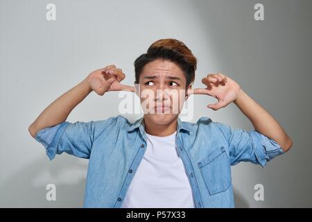 Orinato uomo collegando le orecchie con le dita non vuole ascoltare isolato sul muro grigio sfondo Foto Stock