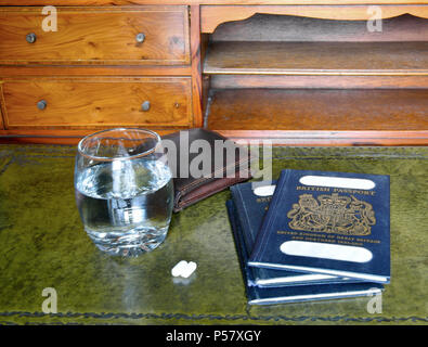Blu passaporto britannico con custodia in cuoio, vetro os acqua e pillole su legni antichi scrivania Foto Stock