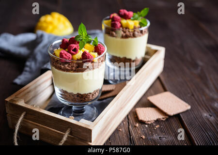 Layered mango dessert con crema di formaggio, biscotti sbriciolati e liofilizzate lamponi servita in vasetti di vetro Foto Stock