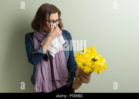 La molla allergia ai pollini. Donna con bouquet di fiori gialli sta per starnutire. Sfondo opaco verde Foto Stock