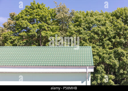 Metallo verde tetto bianco e pioggia sistema di gronda. nuova casa contro i verdi alberi in presenza di luce solare Foto Stock