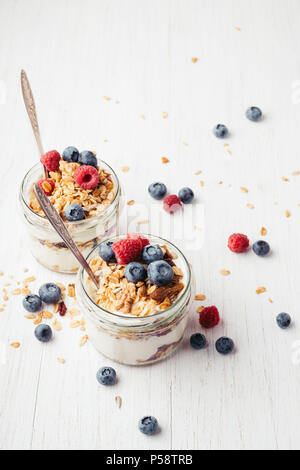 Una sana prima colazione. Due vasi con gustosi parfaits fatta di granola, bacche e yogurt bianco su un tavolo di legno. Girato l'angolo. Foto Stock